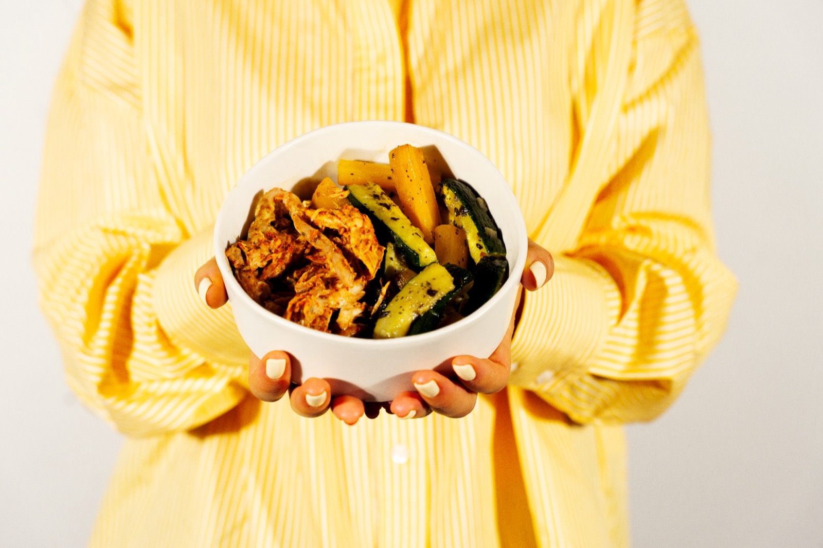 Un bol de poulet effiloché, courgettes et carottes rôties, tenu à deux mains.