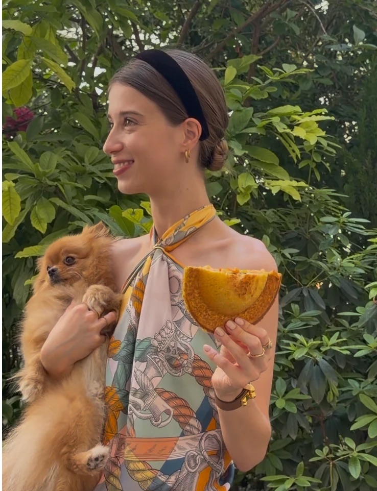 Une invitée souriante tient un Snob et son chien dans un jardin.