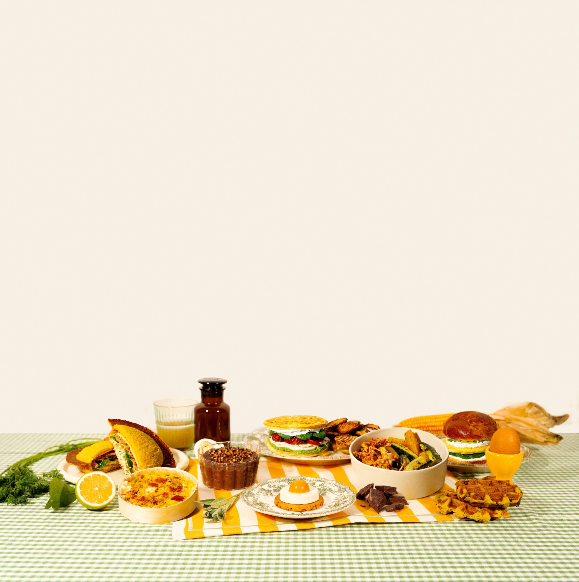La table Domi sur une nappe vichy verte : Snob, quiche sans pâte, mousse au chocolat, Waouhffle, bone broth et bol de poulet, tous dans des contenants ronds.