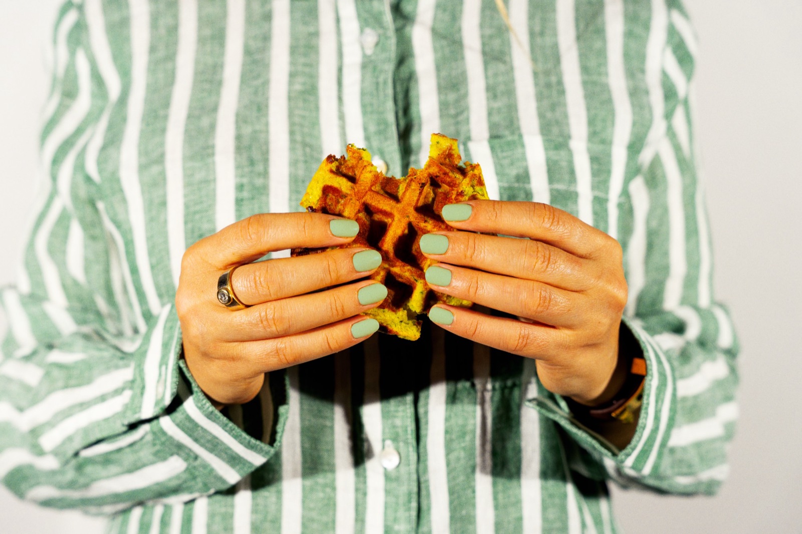 Une Waouhffle aux courgettes croquée, tenue à deux mains.